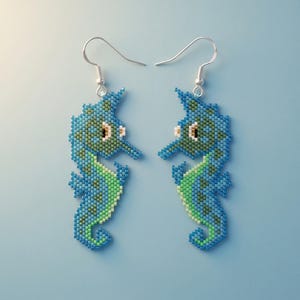 May include: A pair of seahorse-shaped dangle earrings crafted from small beads in shades of blue, green, and white. Each earring features a silver-toned metal hook for attachment, with the seahorse design displaying a detailed pixelated pattern.