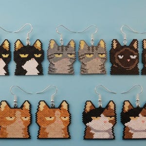 以下が含まれることがあります： 小さなビーズで作られた猫の形のイヤリング5ペア。それぞれ不機嫌そうな表情をしています。黒白、グレーのトラ柄、ダークブラウン、オレンジのトラ柄、三毛猫柄のデザインがあり、すべて銀色のフックに取り付けられています。