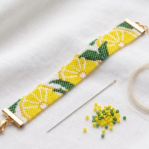 May include: A beaded bracelet featuring a repeating lemon slice pattern in yellow, white, and green. The bracelet has gold-tone metal end caps, a lobster clasp, and an extender chain. A sewing needle, loose yellow and green beads, and clear thread are included.