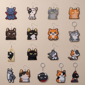 May include: A collection of sixteen cat-themed accessories, including beaded earrings and keychains. The items feature various pixel-art style cat designs in colors like black, white, orange, gray, and calico, each with metal hooks or rings.
