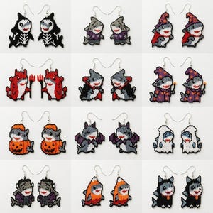 Puede incluir: Una colección de doce pares de pendientes de cuentas con forma de tiburón que lucen varios disfraces, incluyendo esqueletos, calabazas, fantasmas, vampiros, diablos y magos. Cada par está hecho de pequeñas cuentas de colores y cuelga de ganchos de metal plateado.