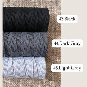 May include: Three spools of macrame cord in black, dark gray, and light gray. The colors are labeled with white text: "43. Black", "44. Dark Gray", and "45. Light Gray". The background is a textured, neutral color.