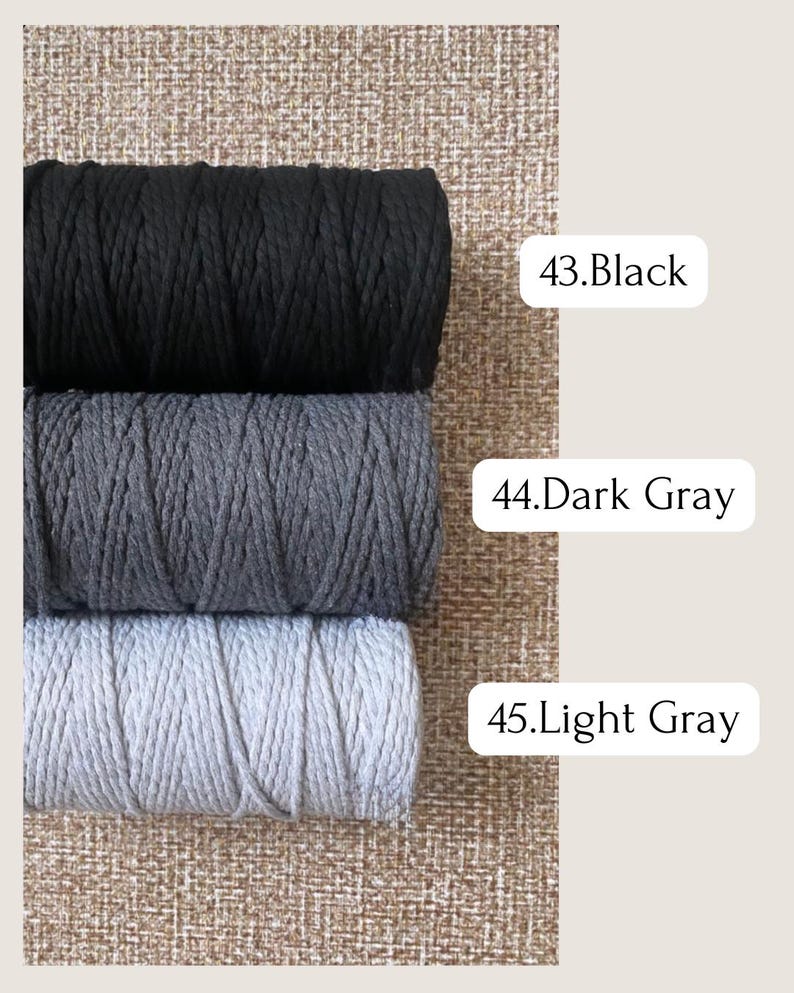May include: Three spools of macrame cord in black, dark gray, and light gray. The colors are labeled with white text: "43. Black", "44. Dark Gray", and "45. Light Gray". The background is a textured, neutral color.