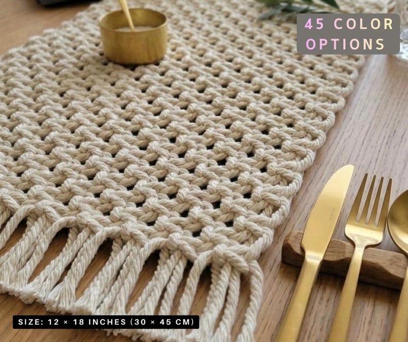 May include: A beige macrame table runner with fringe, measuring 12 x 18 inches. The text "45 COLOR OPTIONS" is visible. Gold-colored cutlery rests on a wooden surface, alongside a small gold bowl.