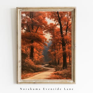 May include: A framed wall art print depicting a winding path through a dense forest filled with vibrant orange and red autumn foliage. The tall, dark tree trunks frame the narrow trail, which leads into a soft, light-filled background.