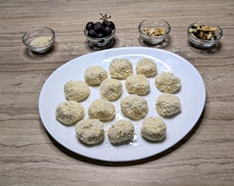 May include: A white oval plate holds a dozen round, breaded food items. Small glass bowls contain grapes, nuts, and rice. The food items are light brown and appear to be coated in a shredded ingredient.