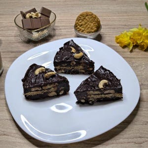 Può includere: Tre fette triangolari di dessert al cioccolato con anacardi su un piatto bianco. Una piccola ciotola di vetro contiene barrette di cioccolato e anacardi. Un'altra ciotola contiene un biscotto. Fiori gialli sullo sfondo.