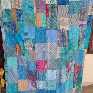 May include: A patchwork quilt in shades of blue, teal, and turquoise. The quilt is made of various fabric squares with different patterns and textures, including floral, geometric, and solid designs. The quilt is hand-stitched with visible thread.