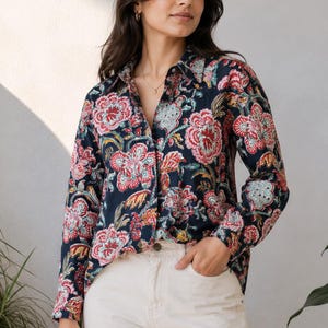 May include: A long-sleeved button-down shirt in a dark navy blue fabric featuring a vibrant floral pattern in shades of red, pink, and light blue. The shirt has a classic collar, a front button placket, and is paired with light beige trousers.