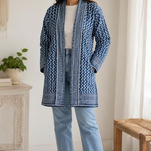 Op de afbeelding: Een jas met lange mouwen en open voorzijde in diepblauw met een wit zigzag- en geometrisch patroon. Het kledingstuk heeft een gestructureerde kraag, een rechte zoom en twee zijzakken, gedragen over een wit topje en een lichtblauwe spijkerbroek met witte sneakers.
