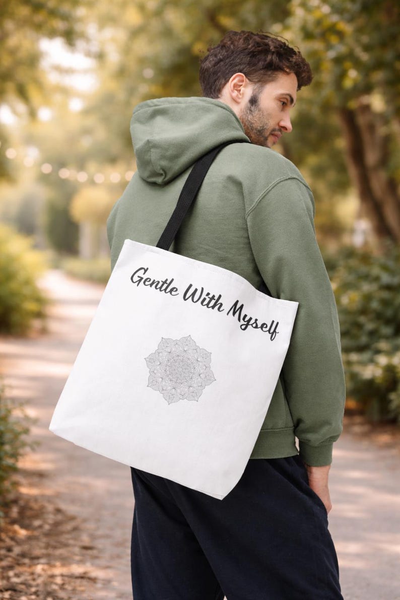 K&ouml;nnte beinhalten: Wei&szlig;e Tragetasche mit dem Text "Gentle With Myself" und einem Mandala-Design. Die Tasche hat einen schwarzen Riemen und wird &uuml;ber der Schulter getragen. Der Hintergrund ist eine verschwommene Au&szlig;enszene.