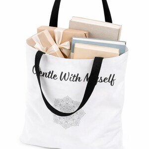K&ouml;nnte beinhalten: Wei&szlig;e Tragetasche mit schwarzen Henkeln, gef&uuml;llt mit B&uuml;chern und verpackten Geschenken. Die Tasche tr&auml;gt den Schriftzug "Gentle With Myself" in Schreibschrift sowie ein detailliertes Mandala-Design am unteren Rand.