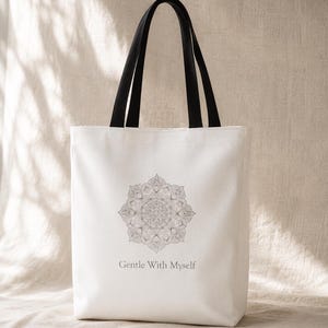 K&ouml;nnte beinhalten: Wei&szlig;er Shopper mit schwarzen Henkeln. Die Tasche hat ein detailliertes graues Mandala-Design und den Text "Gentle With Myself" darunter. Die Tasche ist aus einem hellfarbigen Stoff gefertigt.