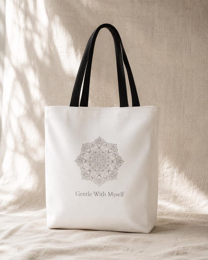 K&ouml;nnte beinhalten: Wei&szlig;er Shopper mit schwarzen Henkeln. Die Tasche hat ein detailliertes graues Mandala-Design und den Text "Gentle With Myself" darunter. Die Tasche ist aus einem hellfarbigen Stoff gefertigt.