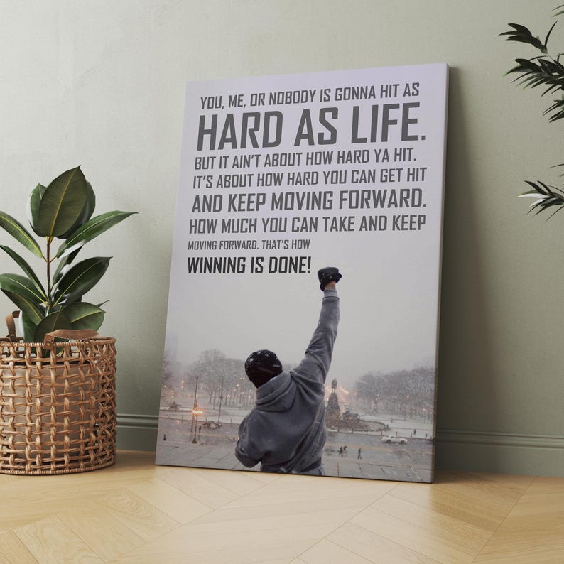 May include: A rectangular wall art print featuring a person in a grey hooded sweatshirt with one arm raised in the air. The background shows a snowy park scene. The text reads: YOU, ME, OR NOBODY IS GONNA HIT AS HARD AS LIFE. THAT'S HOW WINNING IS DONE!