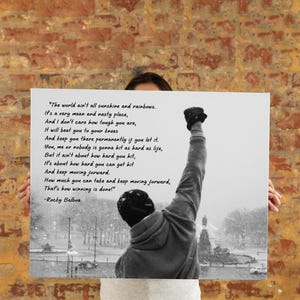 May include: Black and white print featuring a silhouette of a person with their fist raised in the air. The print includes a quote from Rocky Balboa about life's challenges and perseverance. The background shows a snowy outdoor scene.
