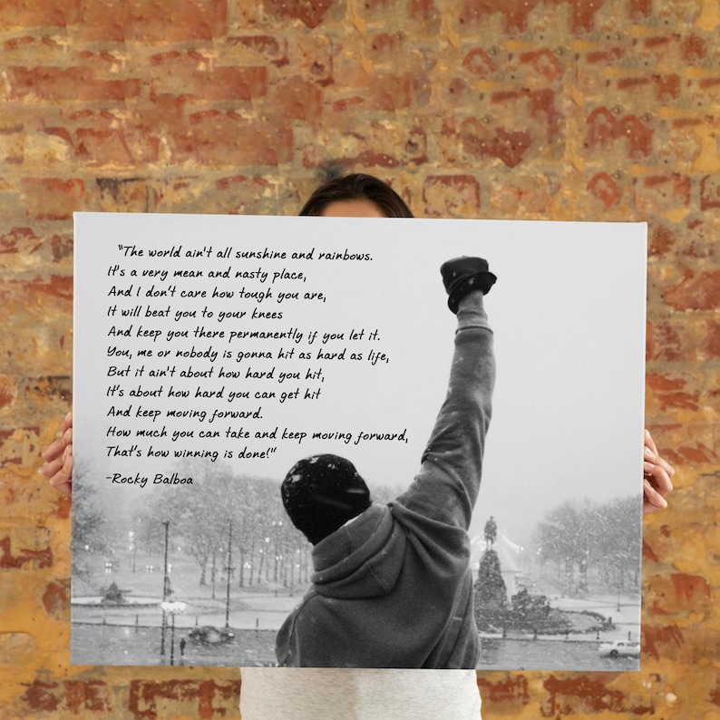 May include: Black and white print featuring a silhouette of a person with their fist raised in the air. The print includes a quote from Rocky Balboa about life's challenges and perseverance. The background shows a snowy outdoor scene.