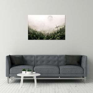 May include: A rectangular wall art print depicting a dense forest landscape shrouded in thick white fog. A pale, circular moon hangs in the upper center sky above the dark green pine trees, with a faint silhouette of a structure visible.