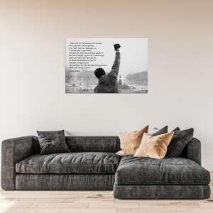 May include: Black and white wall art featuring a motivational quote and an image of a person with their fist raised in the air. The quote reads, "The world ain't all sunshine and rainbows..." and is attributed to Rocky Balboa.