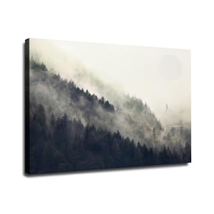 May include: A rectangular canvas wall art print featuring a dense forest of dark green pine trees shrouded in thick, swirling white mist. A pale, circular sun is visible in the upper right sky, with two birds flying near the tree line.