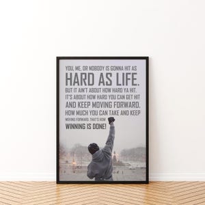 May include: A framed vertical poster featuring a person in a grey hooded sweatshirt with one arm raised in a snowy outdoor setting. The text reads: YOU, ME, OR NOBODY IS GONNA HIT AS HARD AS LIFE. BUT IT AIN'T ABOUT HOW HARD YA HIT. IT'S ABOUT HOW HARD YOU CAN GET HIT AND KEEP MOVING FORWARD. HOW MUCH YOU CAN TAKE AND KEEP MOVING FORWARD. THAT'S HOW WINNING IS DONE!