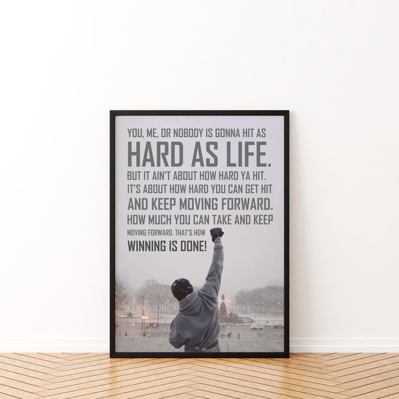 May include: A framed vertical poster featuring a person in a grey hooded sweatshirt with one arm raised in a snowy outdoor setting. The text reads: YOU, ME, OR NOBODY IS GONNA HIT AS HARD AS LIFE. BUT IT AIN'T ABOUT HOW HARD YA HIT. IT'S ABOUT HOW HARD YOU CAN GET HIT AND KEEP MOVING FORWARD. HOW MUCH YOU CAN TAKE AND KEEP MOVING FORWARD. THAT'S HOW WINNING IS DONE!