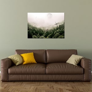 May include: A rectangular wall art print featuring a dense forest landscape shrouded in thick white fog. A pale, circular moon hangs in the upper sky above the dark green treetops, with a faint, sharp structure visible emerging from the mist.
