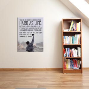 May include: A rectangular wall art print featuring a person in a grey hooded sweatshirt with one arm raised in the air. The print includes the text: YOU, ME, OR NOBODY IS GONNA HIT AS HARD AS LIFE. BUT IT AINT ABOUT HOW HARD YA HIT. IT IS ABOUT HOW HARD YOU CAN GET HIT AND KEEP MOVING FORWARD. HOW MUCH YOU CAN TAKE AND KEEP MOVING FORWARD. THAT IS HOW WINNING IS DONE!