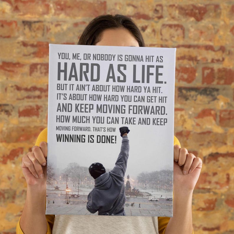 May include: A rectangular canvas print featuring a grey and white background with the text: YOU, ME, OR NOBODY IS GONNA HIT AS HARD AS LIFE. BUT IT AIN'T ABOUT HOW HARD YA HIT. IT'S ABOUT HOW HARD YOU CAN GET HIT AND KEEP MOVING FORWARD. THAT'S HOW WINNING IS DONE!
