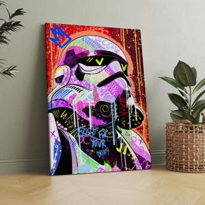 May include: A vibrant canvas print featuring a stylized Stormtrooper helmet with graffiti-style art. The artwork incorporates bright colors like pink, purple, and yellow, with the words "FIGHT FOR YOUR DREAMS" visible. A blue crown and the word "ICON" are also present.
