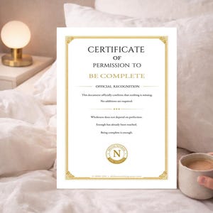 May include: A certificate with gold trim and text that reads "Certificate of Permission to Be Complete." The document includes the text "Official Recognition" and other inspirational phrases. A cup of coffee sits nearby.