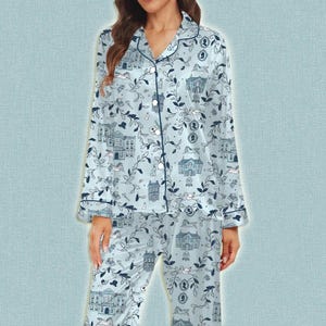 May include: Light blue pajama set with a repeating pattern of buildings, leaves, and animals. The long-sleeved top has a collared neckline and button-down front. The pajama pants have an elastic waistband. The set is made of a soft, silky material.