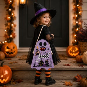 May include: A light purple ghost-shaped Halloween candy bag featuring a cutout window, the name Jacob, and illustrations of a witch, a black cat, a haunted house, and bats. The bag has thick white rope straps and is worn over the shoulder.