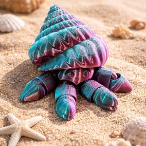 May include: A vibrant 3D-printed crab sculpture, featuring a teal, purple, and pink colour scheme, sits on sand. The crab has a detailed spiral shell and multiple legs. Seashells and a starfish are also visible in the scene.