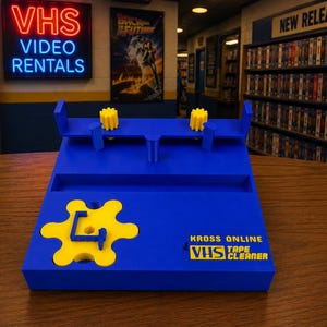 May include: A blue and yellow VHS tape cleaner with the text "Kross Online VHS Tape Cleaner." The cleaner has a unique design with yellow gears and a distinctive shape, perfect for retro video enthusiasts.
