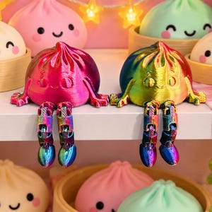 May include: Two articulated dumpling figurines with smiling faces and dangling legs. One figure features a metallic magenta and purple gradient finish, while the other displays a vibrant rainbow spectrum. Both are positioned on a shelf.