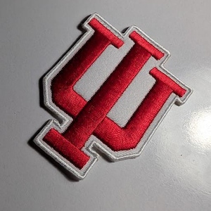 May include: Embroidered patch featuring a red and white design. The patch has a red "IU" logo, with a white background and a white border. The patch is likely for apparel or accessories, and is a collegiate item.