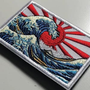 May include: Embroidered patch featuring a stylized depiction of a large ocean wave with a red sun in the background. The wave is rendered in shades of blue, white, and gold, with the sun radiating red lines. The patch has a white border.