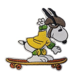 Puede incluir: Parche bordado con Snoopy montando en monopatín. Snoopy lleva una chaqueta amarilla, guantes verdes y un sombrero marrón. El monopatín es marrón con ruedas naranjas. El parche tiene un borde blanco.