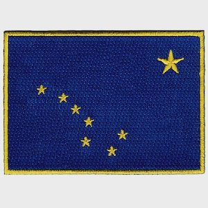Könnte beinhalten: Gestickter Aufnäher mit der Flagge von Alaska. Der Aufnäher hat einen dunkelblauen Hintergrund mit einer Konstellation aus acht goldenen Sternen und einem einzelnen größeren goldenen Stern in der oberen rechten Ecke. Der Rand ist gelb.