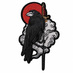 May include: Embroidered patch featuring a black raven perched on a sword, set against a red sun and white cloud design. The raven has a white beak and is detailed with black thread. The patch has a decorative border.