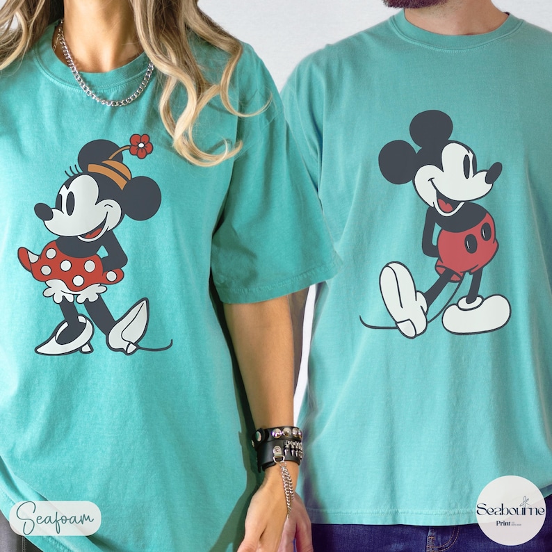 May include: Seafoam green t-shirts featuring Mickey and Minnie Mouse. Minnie is wearing a red polka dot dress and a flower on her head. Mickey is wearing red shorts. The shirts have the words "Seafom" and "Seabourne Print" printed on them.