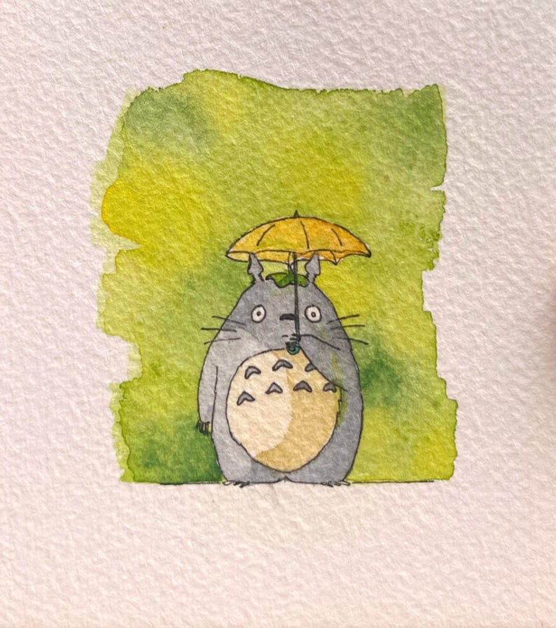 May include: Watercolour painting of a grey Totoro character holding a yellow umbrella. The character has a cream-coloured belly and is set against a green and yellow watercolour background. The artwork is on white paper.