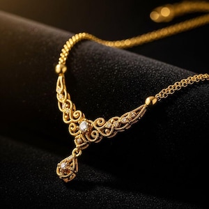 May include: A gold necklace with an ornate design featuring a central pendant and delicate chain. The necklace has a filigree pattern with small, sparkling gemstones. The background is a dark, solid color.