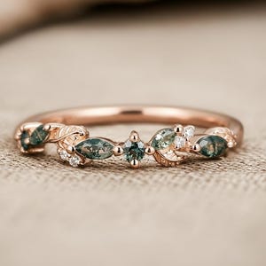 Puede incluir: Anillo de oro rosa con un diseño de hojas y piedras preciosas. El anillo presenta piedras verdes de talla marquesa y redonda, junto con pequeñas piedras blancas. La banda del anillo tiene un acabado pulido, y el diseño general es elegante e inspirado en la naturaleza.