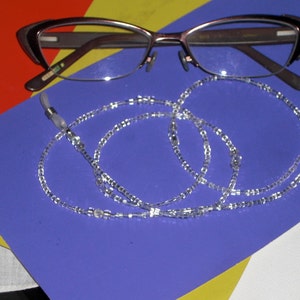 May include: Eyeglasses with a brown frame and a clear beaded eyeglass chain. The glasses are resting on a blue surface, with a red, yellow, and white background.