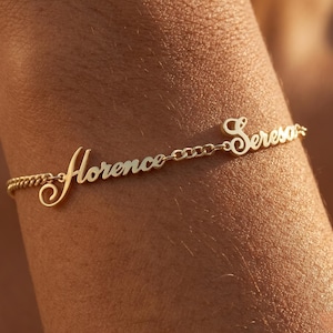 May include: A gold-colored bracelet with the names "Florence" and "Seresa" in a cursive font. The bracelet is attached to a delicate chain. The names are connected by a small chain.