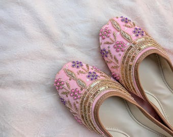 Op de afbeelding: Een paar roze geborduurde ballerina's met gouden en paarse bloemmotieven. De schoenen hebben een lichtbruine rand en zijn versierd met pailletten. De ballerina's zijn waarschijnlijk voor casual wear.