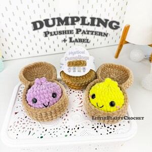 May include: Two crocheted plushies, one purple and one yellow, each with black safety eyes and a stitched smile, nestled inside tan crocheted baskets. A circular product label reads Mystical Dumplings, and text above reads DUMPLING Plushie Pattern + Label.