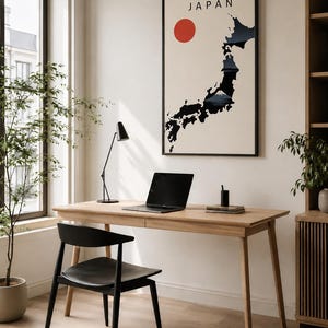 May include: A minimalist home office setup featuring a light wood desk, black chair, and a framed poster of Japan. The poster displays a map of Japan with a red sun and the word "JAPAN". A laptop, lamp, and stationery are on the desk.
